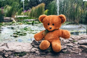 Teddy bear seated next to a pond