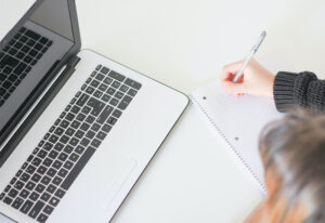 Woman taking notes in notebook in front of a laptop