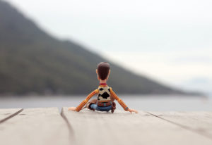 Figurine on Woody from Toy Story looking on a dock looking out over a lake