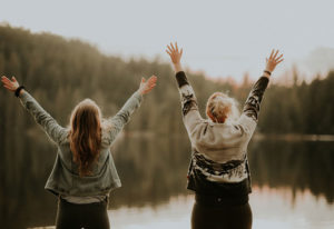 Two women with hands in the air in front of a lake