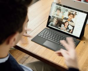 Over the shoulder view of a man participating in a video conference while throwing double peace signs.